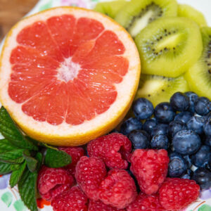 A colourful assortment of fresh grapefruit, kiwi slices, blueberries, raspberries, and mint leaves on a floral-patterned plate, illustrating vibrant food choices for personalised nutrition
