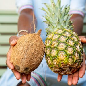 A close-up of Vivene holding out a fresh pineapple and coconut, highlighting natural, whole-food choices essential for personalised nutrition