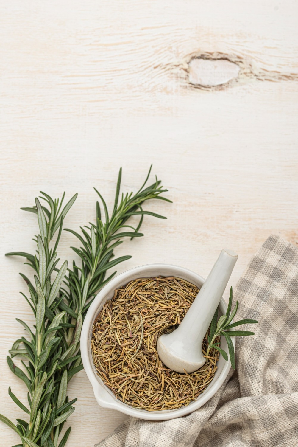 fresh and fry Rosemary on a a table. The dried rosemary is in a mortal and pestal ready to grind up for a nutrition coaching example